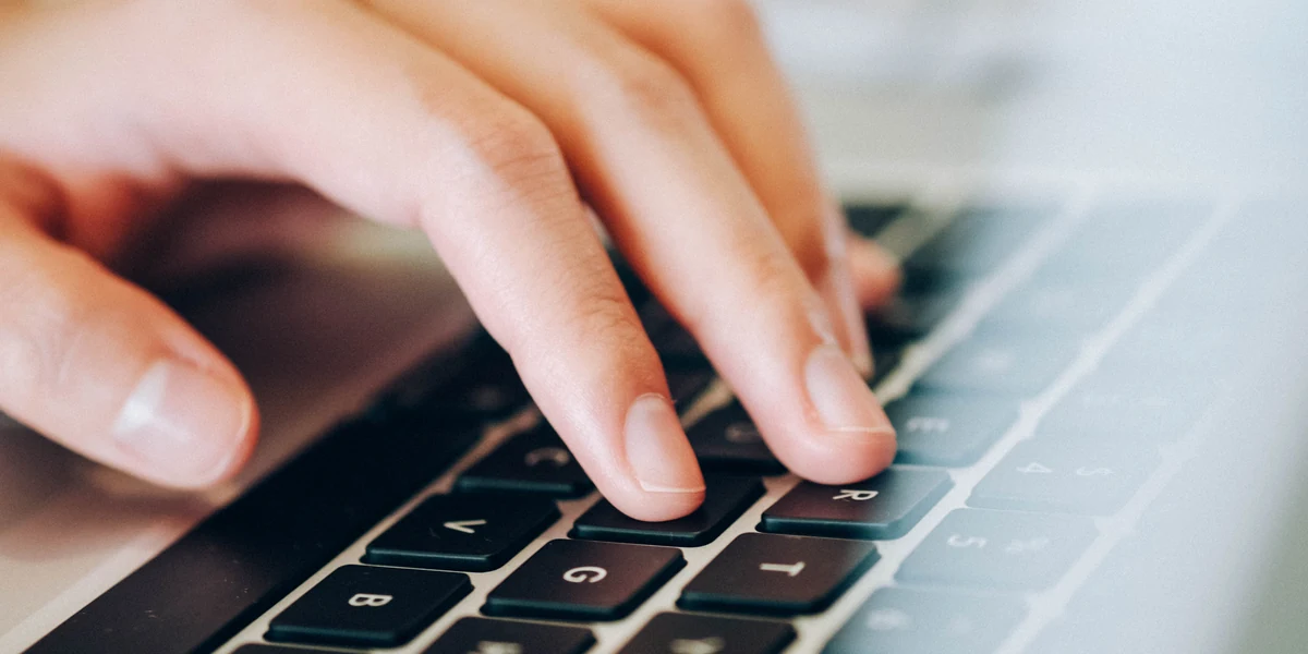 Close-up of a hand resting on a laptop keyboard, with the lit screen just above the keys